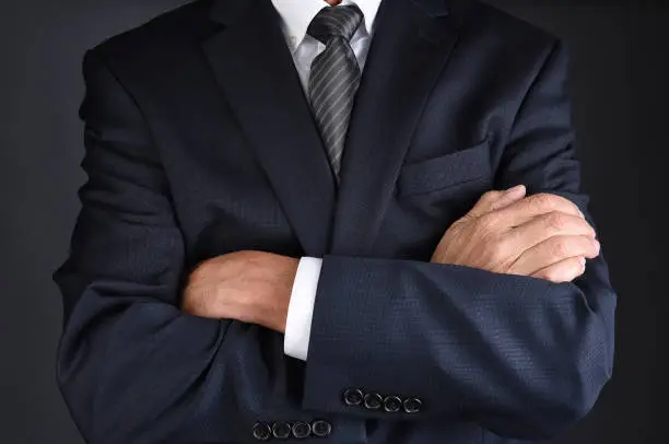 Closeup of a man in a gray business suit with his arms crossed, man is unecognizable.