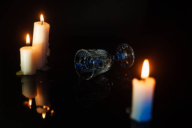 istock Overturned crystal glass laying on a dark mirror table between candles, profile view. Feast or celebration concept 1283596750