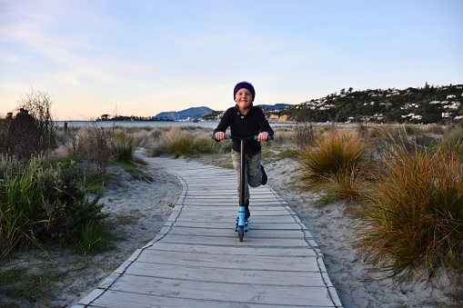 A boy scooters along a boardwalk path at a beach in winter.