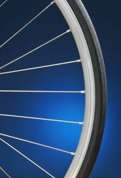 Closeup of a bicycle wheel on a light to dark blue background. Only half of the wheel is shown. Vertical format.