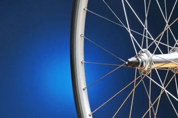Closeup of a bicycle wheel on a light to dark blue background. Only half of the wheel is shown. Horizontal format with copy space.