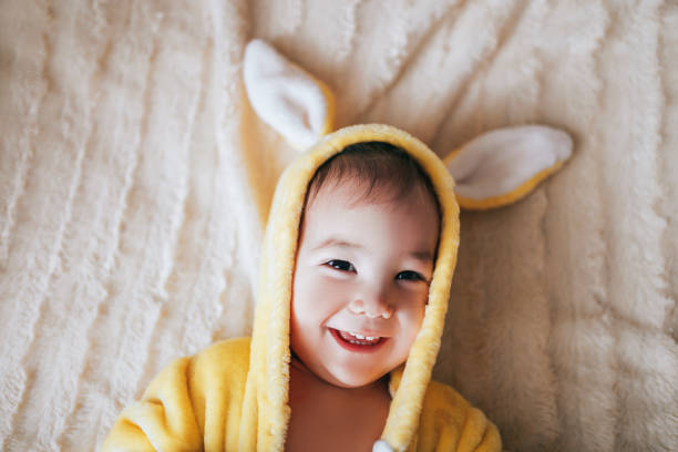 A small child with a rabbit costume. Lying on bad. Yellow rabbit with eggs in hands.