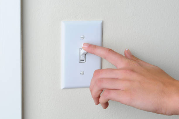 Woman turning off light switch Womans hand with finger on light switch, about to turn off the lights. Closeup of hand and switch only. Horizontal format. light switch stock pictures, royalty-free photos & images