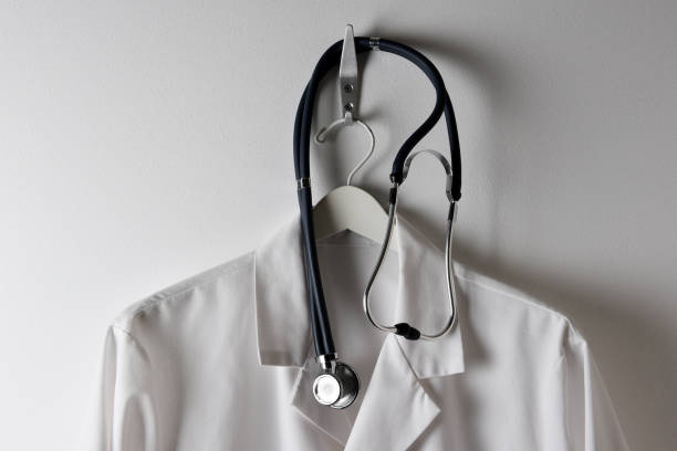 istock Closeup of a Doctors White Lab Coat Hanging on a Hook with Stethoscope, horizontal. 1283603914