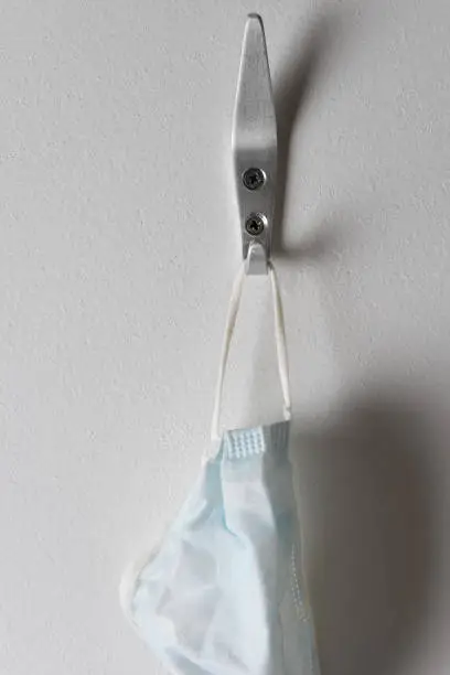 Closeup of a surgical mask hanging from a hook on a wall.