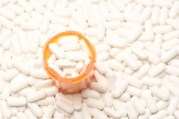 High angle view of a prescription bottled filled with pills surrounded by more of the same tablets Opioid Crisis Concept: High angle view of a prescription bottled filled with pills surrounded by more of the same tablets, with copy space, fentanyl stock pictures, royalty-free photos & images
