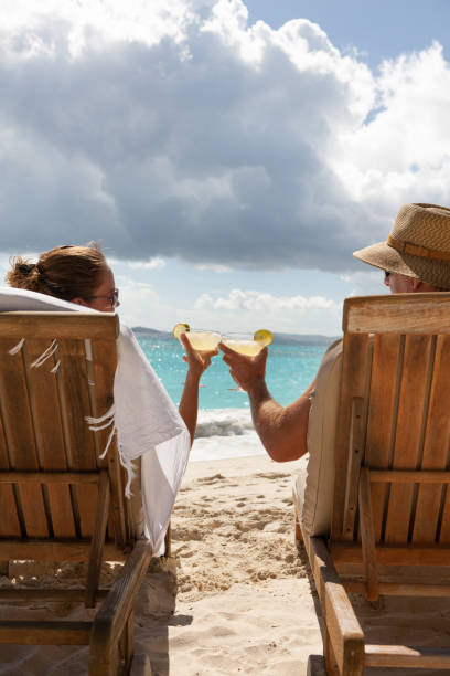 couples triant avec le cocktail dans une chaise longue de teck sur une plage tropicale - women sarong beach white photos et images de collection