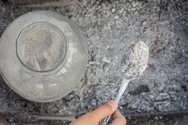 lagerung von holzasche in einem glas, neben einer hand hält einen löffel mit frischer asche - residue stock-fotos und bilder