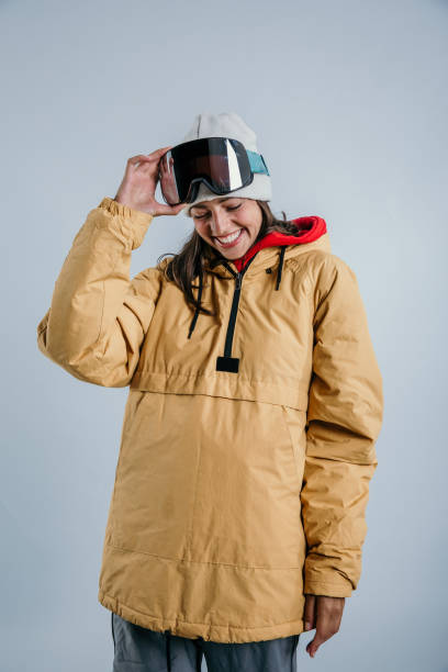 Snowboarder I am Fashion portrait of a sensual young woman in winter outfit - woolen sweater and gloves, fur cap, puffer jacket, and goggle. White blue background. snowboarding snowboard women snow stock pictures, royalty-free photos & images
