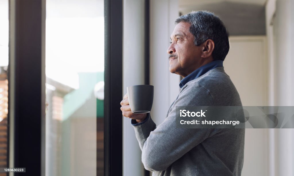There's always something to look forward to Shot of a senior man drinking coffee and looking thoughtfully out of a window Contemplation Stock Photo