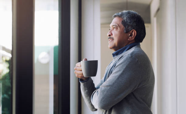 Relax, you did good Shot of a senior man drinking coffee and looking thoughtfully out of a window looking through window stock pictures, royalty-free photos & images