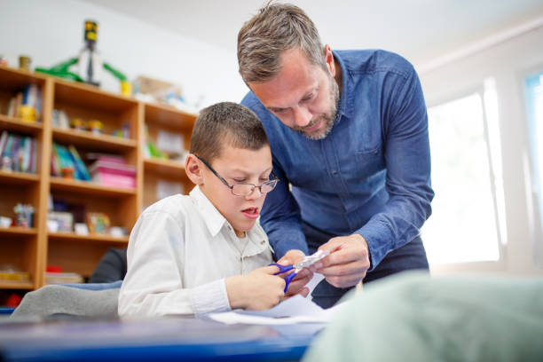 istock Special education teacher showing intellectual disability boy where to cut paper pattern 1283638242