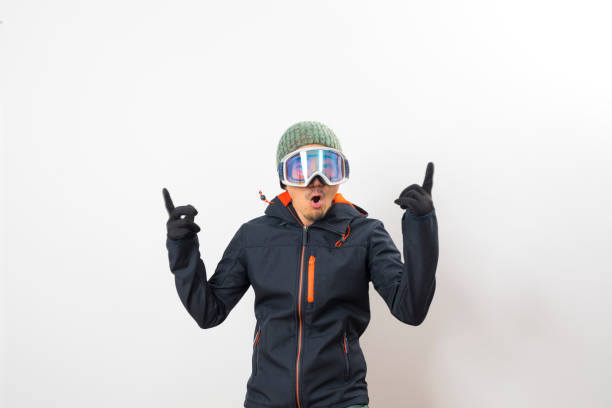 Handsome asian man dressed in winter coat, glove and goggles ready to ski isolated on white background