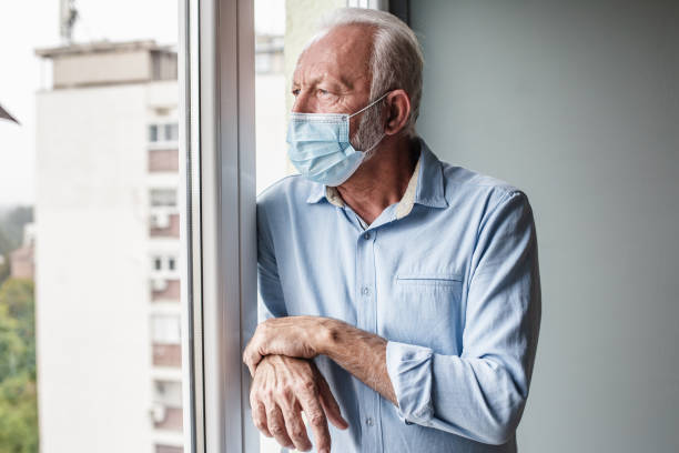 istock Worried senior man with face mask standing by the window 1283665705