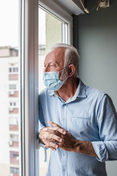 istock Worried senior man with face mask standing by the window 1283666935