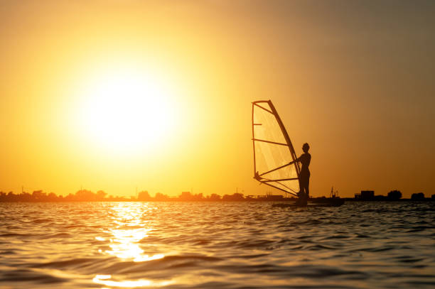 istock A beginner windsurfer woman stands on a board with a sail on a sunset background. Windsurfing school 1283669967