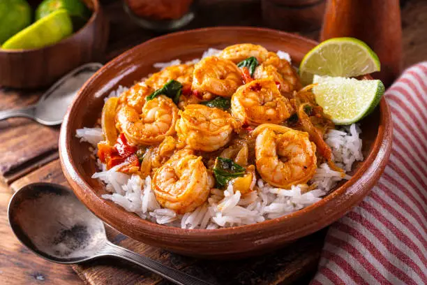 A bowl of delicious south Indian style shrimp curry masala with tomato, spinach,  basmati rice and lime.