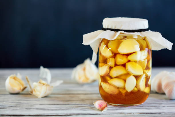 Fermented Garlic Cloves in Honey Fermented garlic cloves in a jar of honey, a rich source of probiotics, over a rustic wood background table. Selective focus with blurred background and foreground. pickled stock pictures, royalty-free photos & images