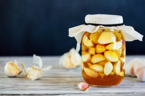 Fermented garlic cloves in a jar of honey, a rich source of probiotics, over a rustic wood background table. Selective focus with blurred background and foreground.