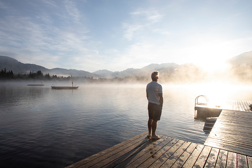 He looks off to distant mountains as mist lifts off water surface