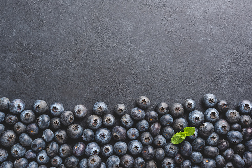 Blueberries as background over black concrete backdrop with copy space for text or design. Top view