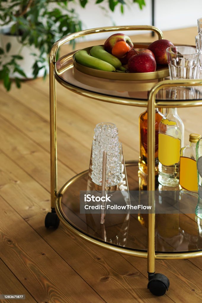 Modern composition of gold kitchen bar with different drinks, fruits, decoration and elegant personal accessories. Template. Modern scandinavian home interior of living room with design retro furniture, tropical plant, window, decoration and elegant personal accessoreis in stylish home decor. Furniture Stock Photo