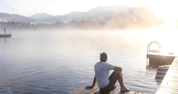 istock Man relaxes on lakeside dock at sunrise 1283672538