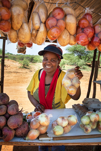 smiling self employed african woman at her street stall selling fresh  vegetables