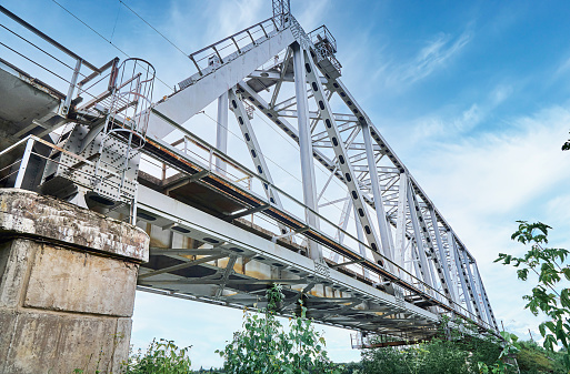 Iron train bridge over the river against a cloudy sky. Bridge in greenery