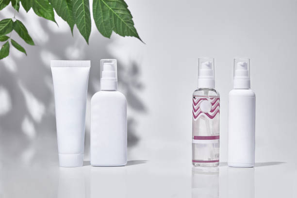 istock Cosmetic tube and three pump bottles with no logo standing on surface against white studio background and green branch. Close up, copy space 1283674439