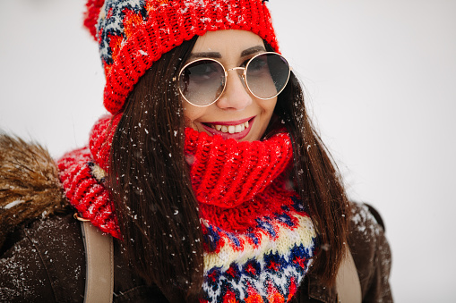 Close up portrait of beautiful young woman in knitted hat and scarf with sunglasses outdoors on snow