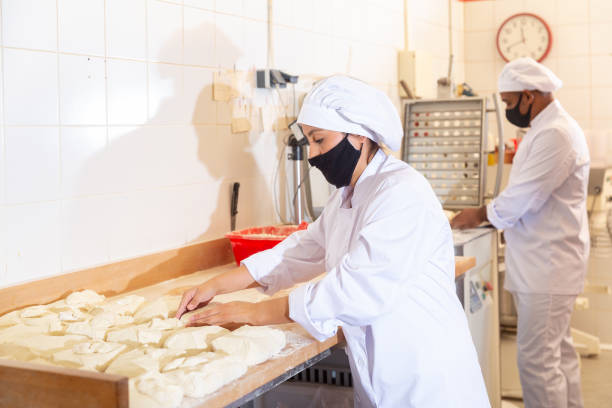 istock Female bakery worker wearing protective mask cuts dough with knife into identical loaves in kitchen 1283675037