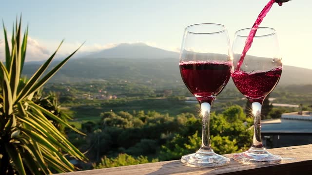 Pouring red wine from a bottle into two glasses on the vineyards in Sicily