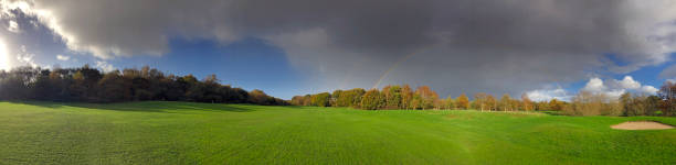 Four seasons in one day as sunshine, autumn colours, storm clouds and a rainbow colour this panorama on the fairway near a bunker at Moors Valley golf course, Dorset, England