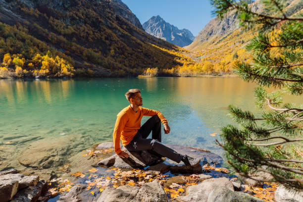 счастливый человек на хрустальном озере в осенних горах. горное озеро и турист - lake alaska mountain mountain range стоковые фото и изображения