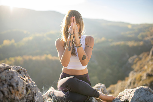 Full shot of a one woman only sitting with cross-leged on the top of the mountain while meditating.