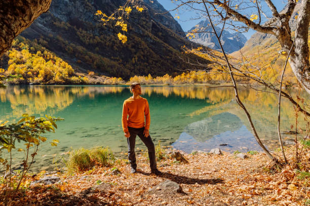счастливый человек на хрустальном озере в осенних горах. горное озеро и турист - lake alaska mountain mountain range стоковые фото и изображения