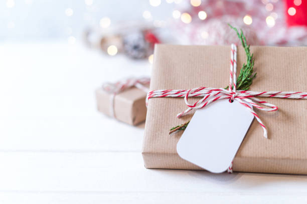 istock Christmas eco gift with empty tag. Glowing snow bokeh, coniferous branch. Winter holidays mock up on white background. Zero waste, plastic free. 1283680731
