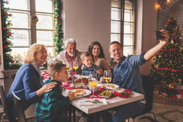 Family taking a selfie during Christmas dinner Beautiful happy family gathered around the table, having Christmas dinner, enjoying their time together and taking a selfie family christmas stock pictures, royalty-free photos & images