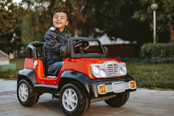 kleiner junge reitet spielzeugauto im garten - spielzeugauto stock-fotos und bilder