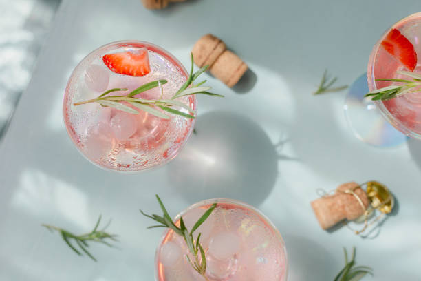 sommergetränk mit weiß wein. hausgemachter erfrischender fruchtcocktail oder punsch mit champagner, erdbeeren, eiswürfeln und rosmarin auf hellblauem hintergrund. - champagne pink strawberry champaigne stock-fotos und bilder