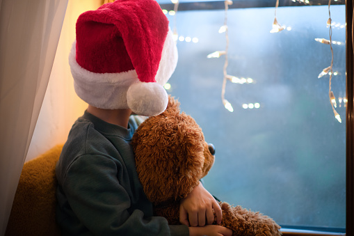 Child indoors playing with his Teddy bear on Christmas during self-isolation and coronavirus COVID-19 pandemic