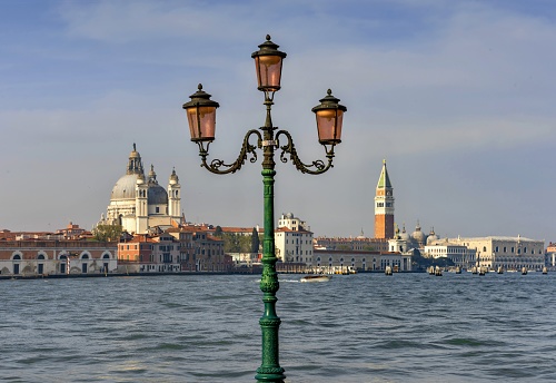 Venice, Italy, April 3, 2016: View of an old street lamp on the island of Giudecca in the Venetian lagoon. In the background is the church of Santa Maria della Salute (left), the St Mark's Campanile and the Doge's Palace (right).