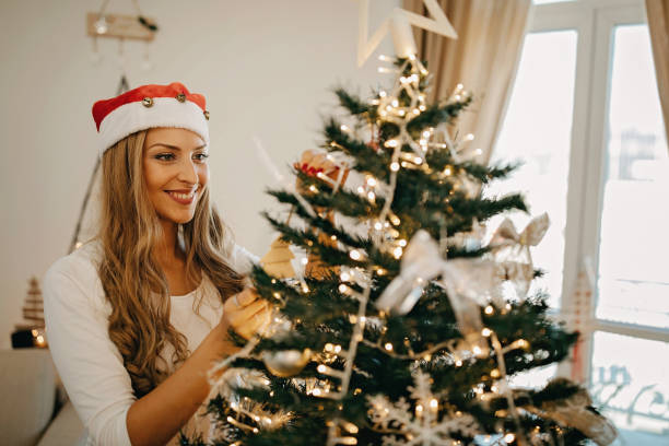 istock Young woman wearing santa hat decorating christmas tree 1283686206