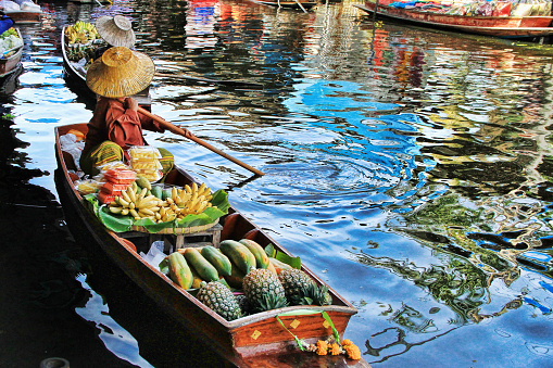 Thai woman in straw hat selling food on boat at floating market in Thailand
