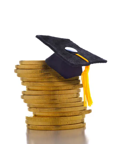 College Admissions Scandal: Mortarboard on a stack of gold coins representing the high cost of education, Student Loans and Bribery.