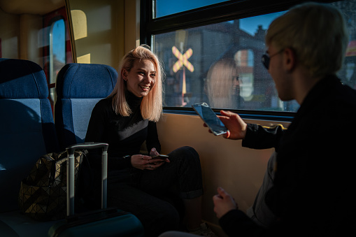 Smiling teenagers are using smart phones while riding in the train.