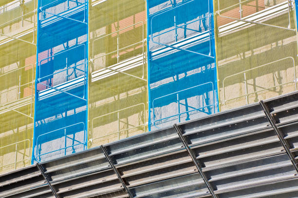 Metal scaffolding on a construction site built with prefabricated components to work safely on the facade of a building for the renovation of the plaster wall or realization of thermal insulation to improve the energy efficiency of the building. andamios metálicos en una obra construida con componentes prefabricados para trabajar de forma segura en la fachada de un edificio para la renovación de la pared de yeso o la realización de aislamiento térmico para mejorar la eficiencia energética del