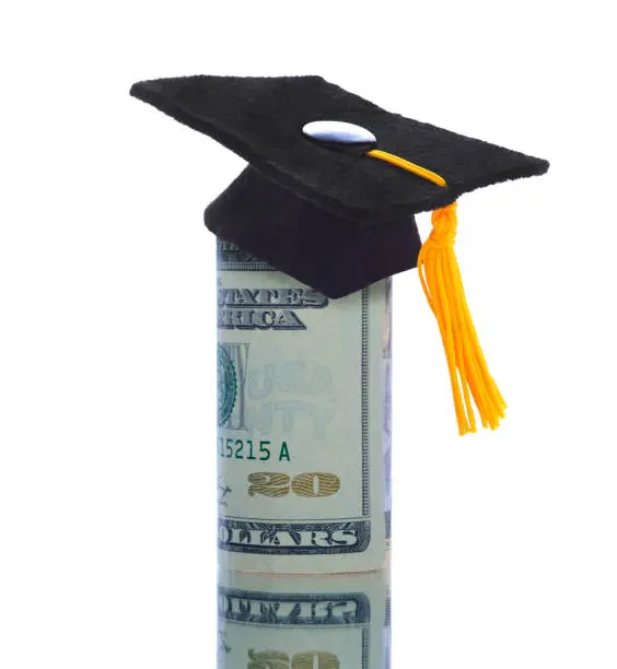 A wad of twenty dollar bills wrapped around themself with a mortarboard ontop depicting the high cost of Education or the College Admission Bribery Scandal.