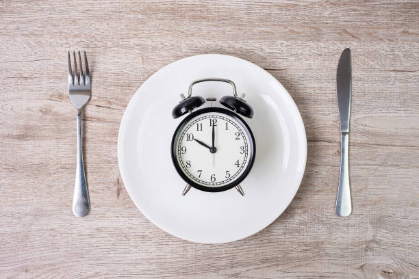 istock knife and fork with alarm clock on white plate on tablecloth background. Intermittent fasting, Ketogenic dieting, weight loss, meal plan and healthy food concept 1283690327